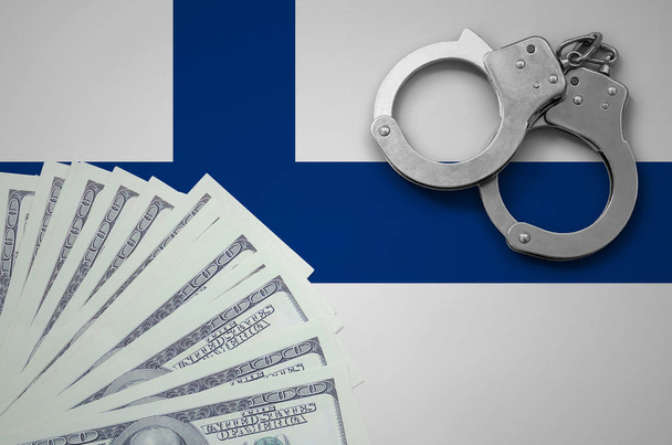 Finland flag  with handcuffs and a bundle of dollars. The concept of illegal banking operations in US currency. - Photo, Image