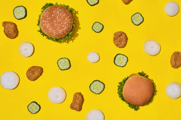 最も人気のあるファーストフードの食事。チキンナ ゲット、新鮮なキュウリと黄色の背景に玉ねぎとハンバーガーのトップ ビュー - 写真・画像