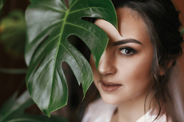 gorgeous bride portrait with monstera leaf. beautiful woman getting ready for wedding, holding green leaf and posing. skin care and make-up. sensual moment - Photo, Image