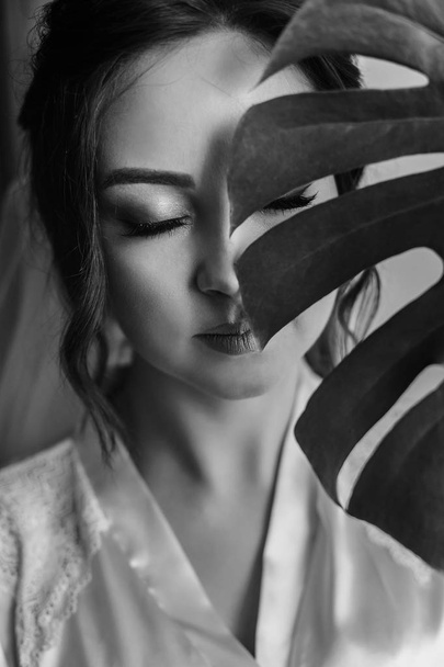gorgeous bride portrait with monstera leaf. beautiful woman getting ready for wedding, holding green leaf and posing. skin care and make-up. sensual moment - Foto, imagen