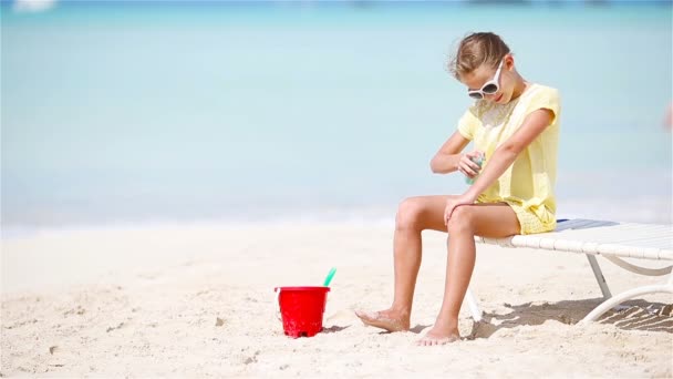 Malá holka s lahví opalovacího krému sedí na tropické pláži - Záběry, video