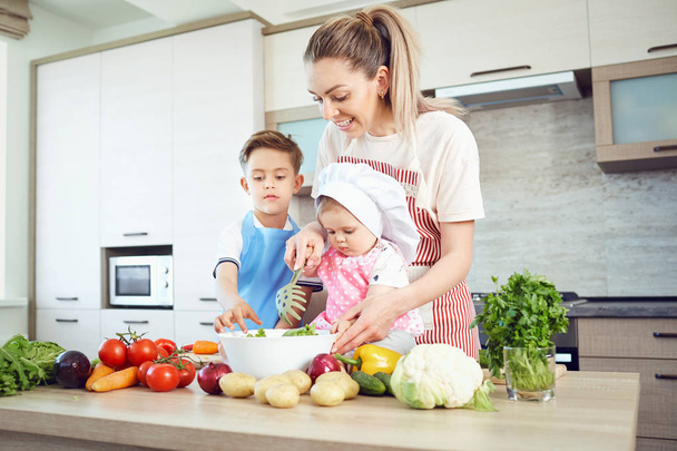 Mother and children are cooking in the kitchen - Фото, изображение