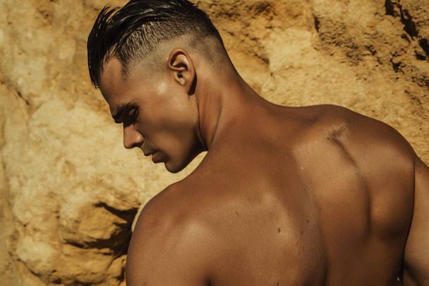 Strong face muscled male model on the nature background with sand rocks  and water on the beach on the sunset - Photo, Image