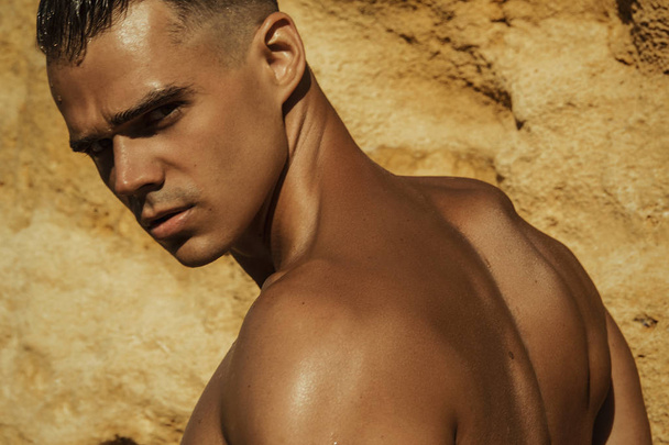 Strong face muscled male model on the nature background with sand rocks  and water on the beach on the sunset - Photo, Image