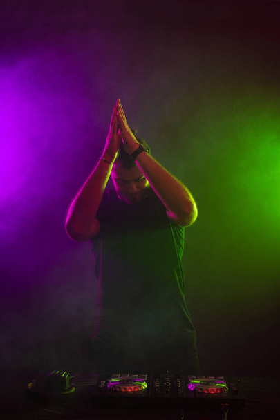 DJ παίζει μουσική στο μίξερ σε πολύχρωμα ομιχλώδες φόντο - Φωτογραφία, εικόνα
