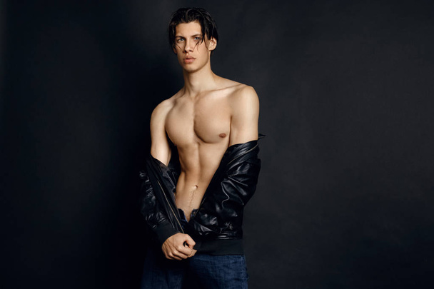 Male model in denim blue jeans and black leather jacket on black background in studio isolated - Фото, зображення