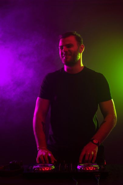 Attractive young DJ playing on turntables with color light effects - Foto, Bild
