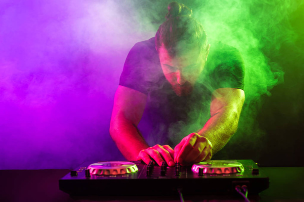 Attractive young DJ playing on turntables with color light effects - Photo, Image