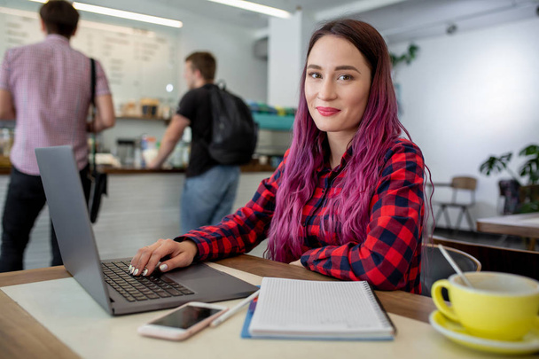Nuori nainen vaaleanpunaiset hiukset kannettavan tietokoneen istuu kahvilassa, älykäs naispuolinen opiskelija työskentelee net-kirja
. - Valokuva, kuva
