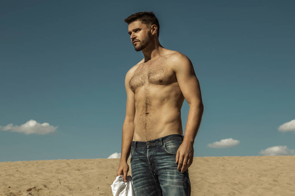 Strong commercial face male model  wearing white sunglesses jeans and white t-shirt  on sand and  blue sky with clouds  - Fotó, kép