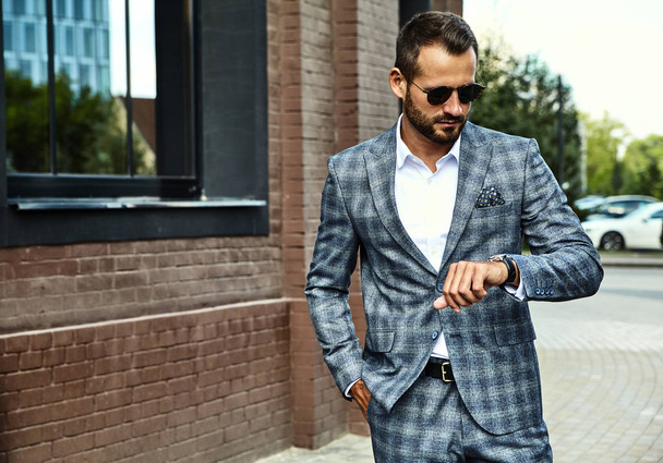 Portrait of sexy handsome fashion businessman model dressed in elegant checkered suit posing on street background. Metrosexual - Foto, Imagen