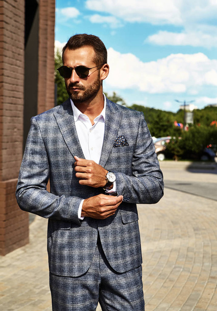 Portrait of sexy handsome fashion businessman model dressed in elegant checkered suit posing on street background. Metrosexual - Foto, afbeelding