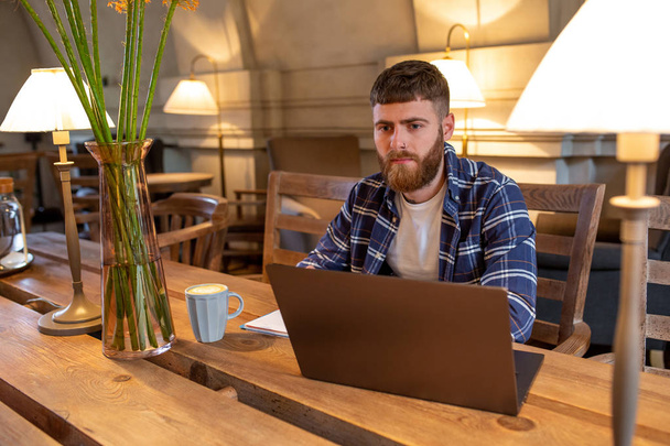 Jonge professional surfen op het Internet op zijn laptop in een café - Foto, afbeelding