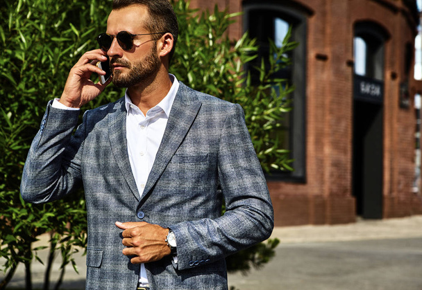 Portrait of sexy handsome fashion businessman model dressed in elegant checkered suit having business mobile conversation on smartphone on street. Metrosexual - Foto, afbeelding