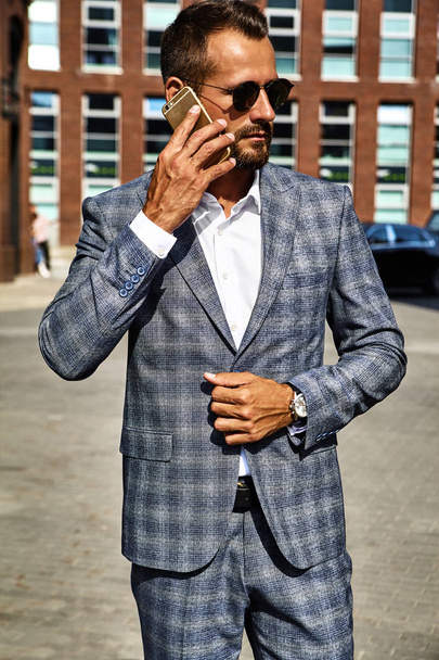 Portrait of sexy handsome fashion businessman model dressed in elegant checkered suit having business mobile conversation on smartphone on street. Metrosexual - Foto, Imagen