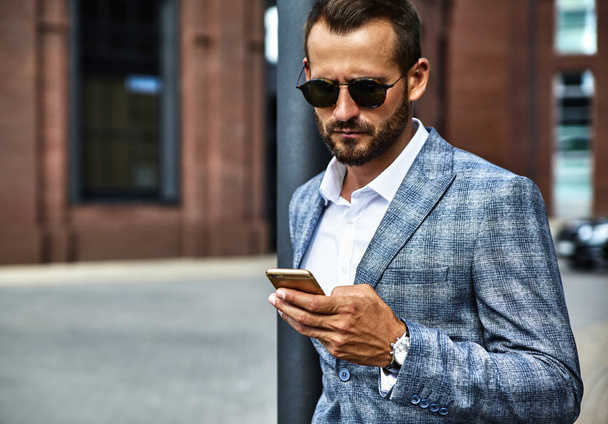 Portrait of sexy handsome fashion businessman model dressed in elegant checkered suit having business mobile conversation on smartphone on street. Metrosexual - Valokuva, kuva