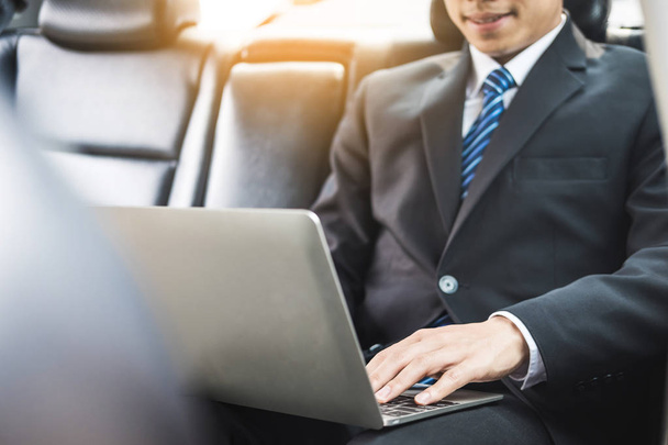 Красивый молодой бизнесмен, использующий ноутбук и сидящий на заднем сидении автомобиля
 - Фото, изображение