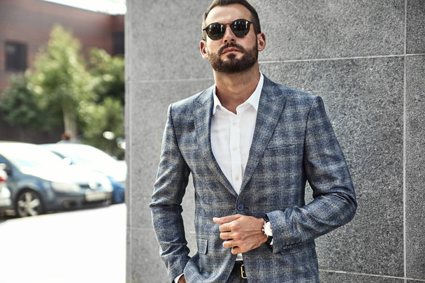 Portrait of sexy handsome fashion businessman model dressed in elegant checkered suit posing near gray wall on street background. Metrosexual - Zdjęcie, obraz