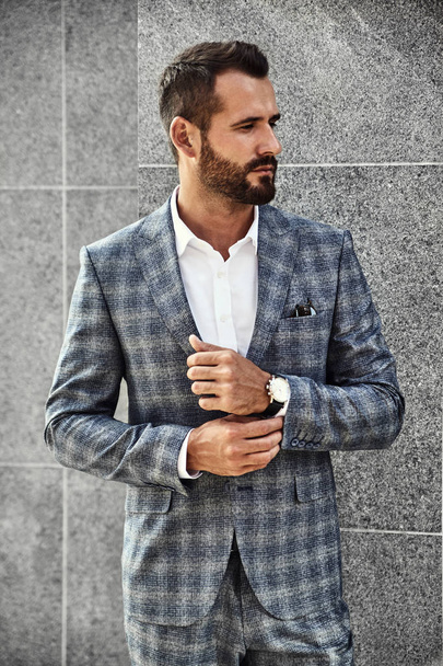 Portrait of sexy handsome fashion businessman model dressed in elegant checkered suit posing near gray wall on street background. Metrosexual - Фото, зображення