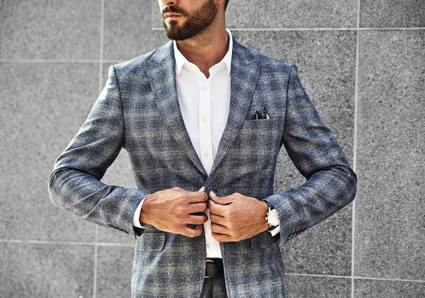 Fashion businessman model dressed in elegant checkered suit posing near gray wall on street background. Metrosexual with luxury watch on wrist - Foto, immagini