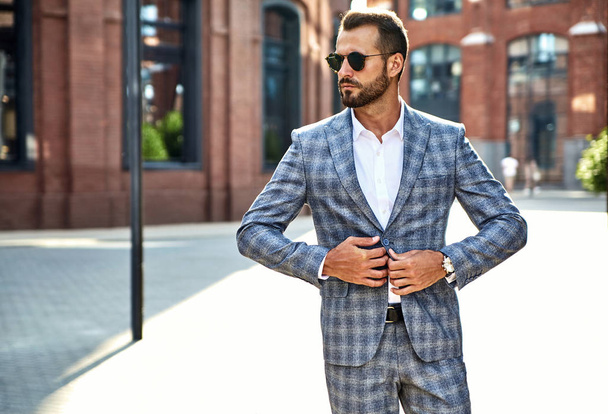 Portrait of sexy handsome fashion businessman model dressed in elegant checkered suit posing on street background. Metrosexual - 写真・画像