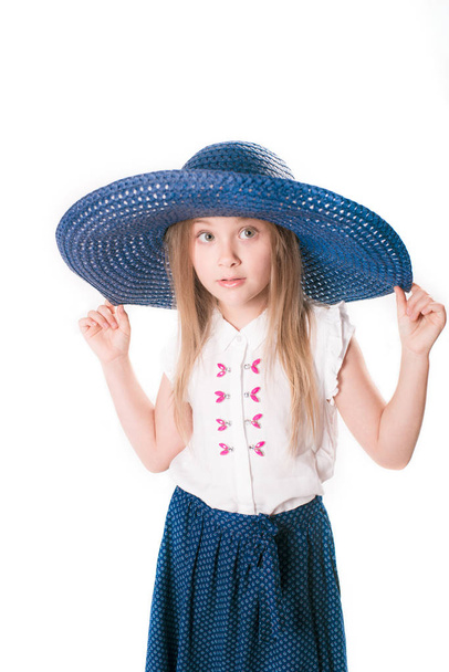 Beautiful fashionable little girl with blond hair in a hat with wide brim and a long fashionable skirt in the studio on a white background - Foto, afbeelding