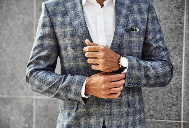 Fashion businessman model dressed in elegant checkered suit posing near gray wall on street background. Metrosexual with luxury watch on wrist - Фото, изображение