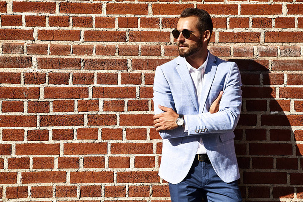 Portrait of sexy handsome fashion businessman model dressed in elegant blue suit posing near brick wall on the street background. Metrosexual - Foto, afbeelding