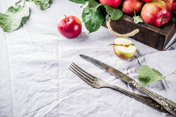 Осенний кулинарный фон с вилкой, ножом, свежие красные яблоки с листьями, на льняной скатерти стол, копировальное место
 - Фото, изображение