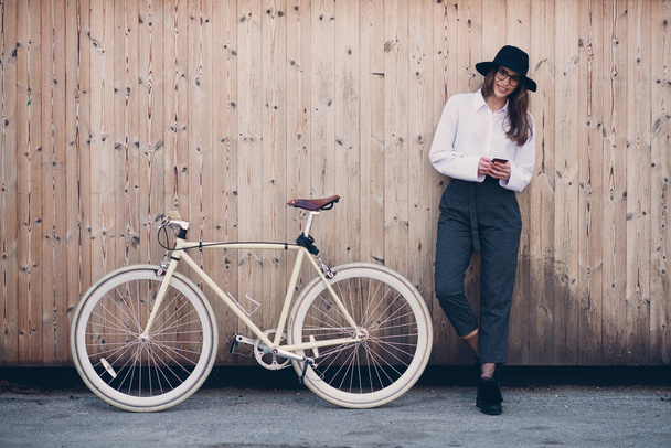 Portrait of beautiful brunette holding bicycle. Wooden background. - 写真・画像