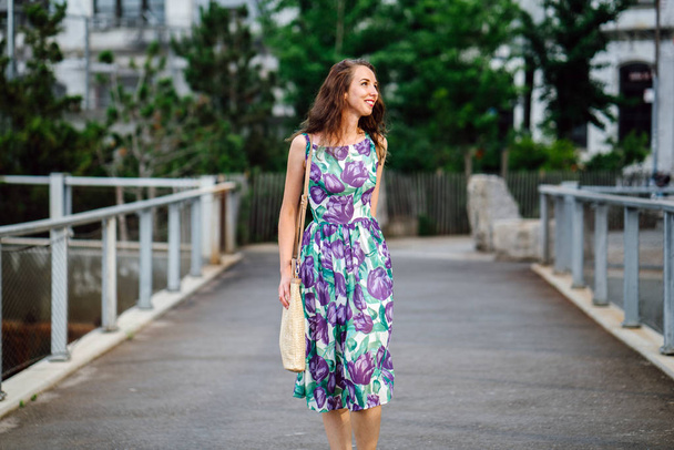 brunette woman with curly hair holding bag walking in green park  - Fotografie, Obrázek