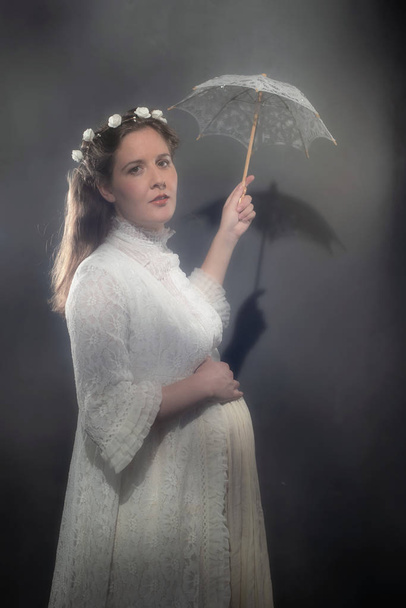 Historické těhotná bruneta žena v bílých šatech hospodářství deštník. - Fotografie, Obrázek