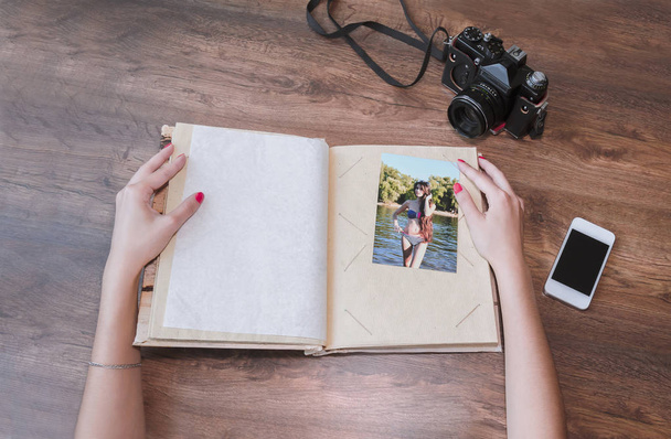 girl's hands and photo album, photo camera, phone on a wooden background, close-up - Foto, Imagem