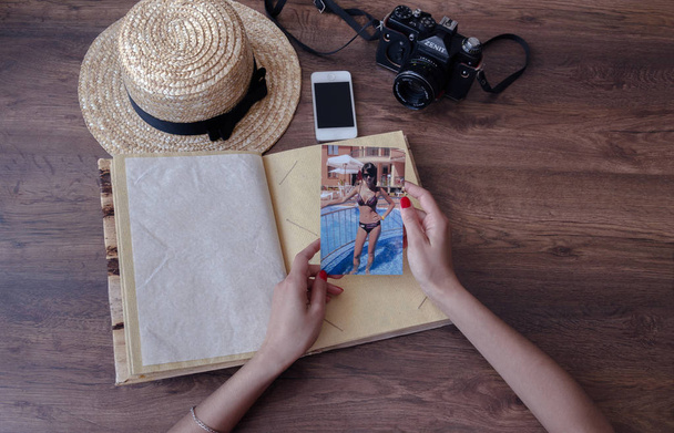 girl's hands and photo album, photo camera, phone, straw hat and on a wooden background, close-up - Photo, Image