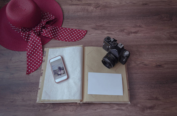 photo album, photo camera, phone and hat on a wooden background, close-up - Photo, Image
