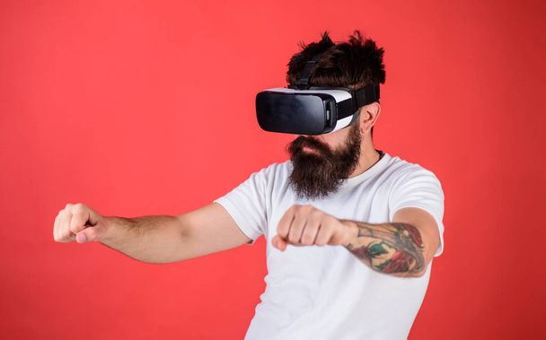 Virtual driving lessons concept. Hipster on confident face driving bike in virtual reality with modern digital gadget. Man with beard in VR glasses driving motorbike, red background - Foto, Imagen