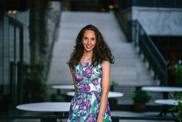 three quarter length portrait of smiling woman with curly hair posing on concrete stairs background - Φωτογραφία, εικόνα