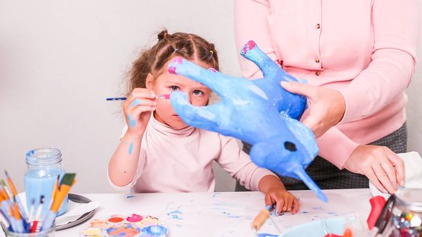 Мать и дочь рисуют бумажный маше единорог с голубой краской вместе
. - Фото, изображение