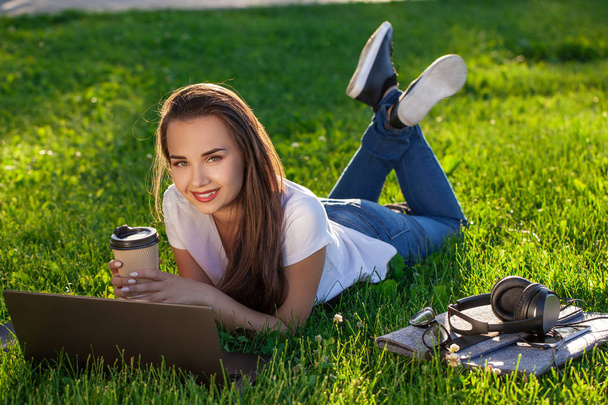 Mujer joven usando el portátil en el parque acostado en la hierba verde. Concepto de actividad del tiempo libre. - Foto, imagen
