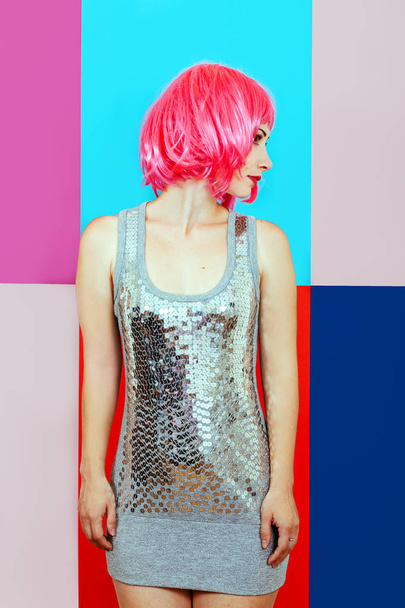 Beautiful girl with pink hair dressed in silver dress on a multicolored graphic background. Portrait of a woman in a deadpen style without emotions. - Photo, Image