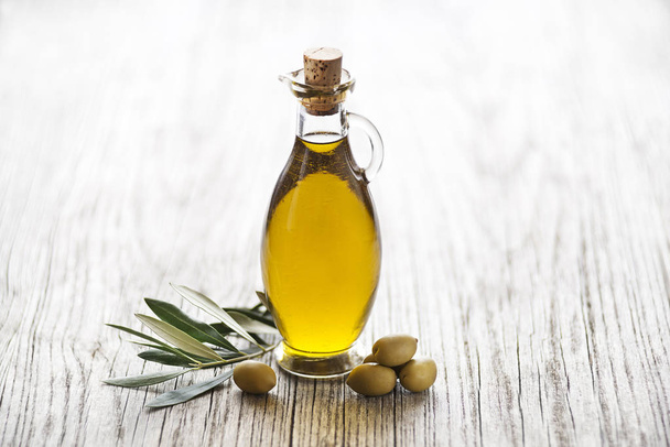 Olive oil with olive branch on wooden table - Fotó, kép