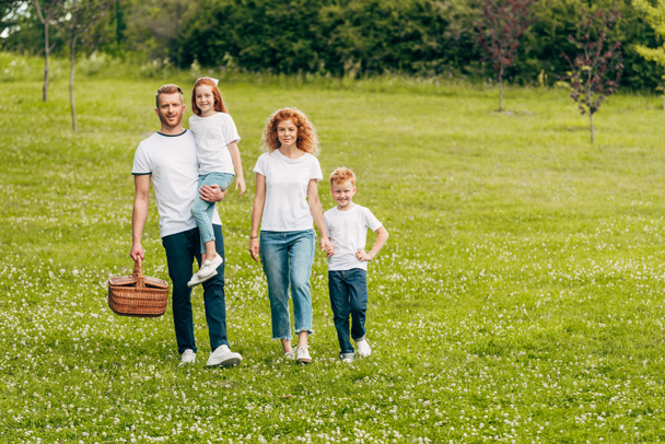 happy family smiling at camera while walking with picnic basket in park  - Foto, immagini