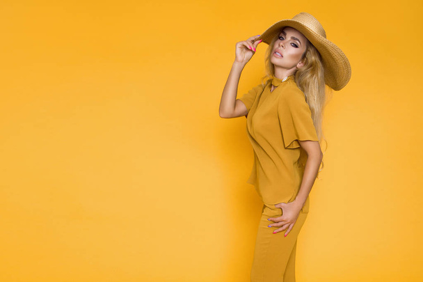 Beautiful, sexy, elegant woman with blond hair poses in studio in elegant yellow clothing and hat. - Photo, image