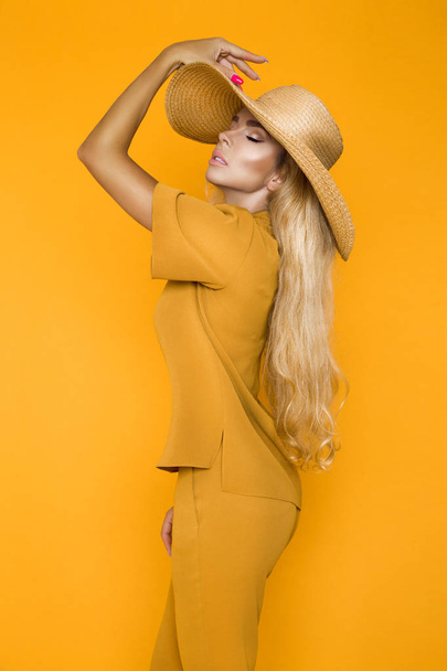 schöne, sexy, elegante Frau mit blonden Haaren posiert im Studio in eleganter gelber Kleidung und Hut. - Foto, Bild