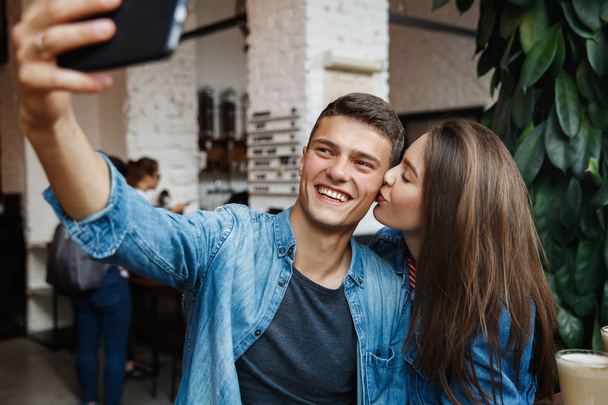 Couple Taking Photos With Coffee In Cafe. Smiling Young Man And Happy Woman Doing Selfie Photo On Mobile Phone While Sitting With Cups Of Coffee At Table In Coffee Shop. High Resolution. - Fotografie, Obrázek