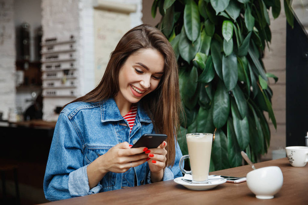Молода жінка пише смс або користується смартфоном і п "є каву в кафе, міському житті, кафе життя, сучасне життя. - Фото, зображення