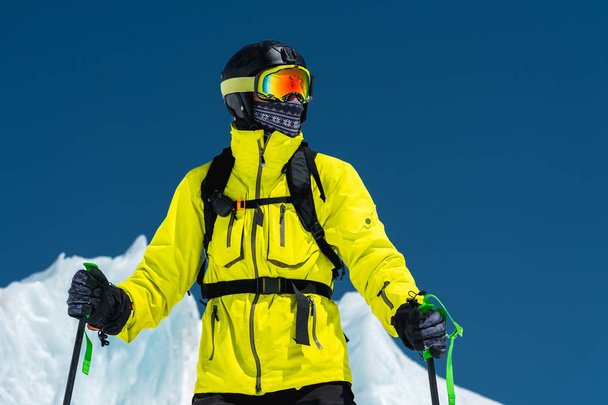 Skier standing on a slope. Man in a light suit, the helmet and mask in skiing is to ski. In the background snow-capped mountains , skiers . Caucasus Mountains, Elbrus, Russia - Photo, image