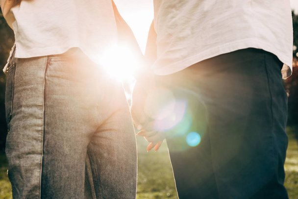 cropped shot of young couple holding hands while standing together in park at sunset - Fotoğraf, Görsel