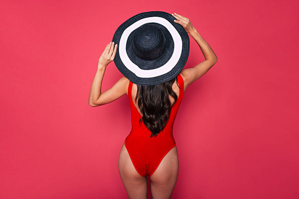 Rear view of young woman in colorful stylish swimsuit and hat on blue background - Fotografie, Obrázek