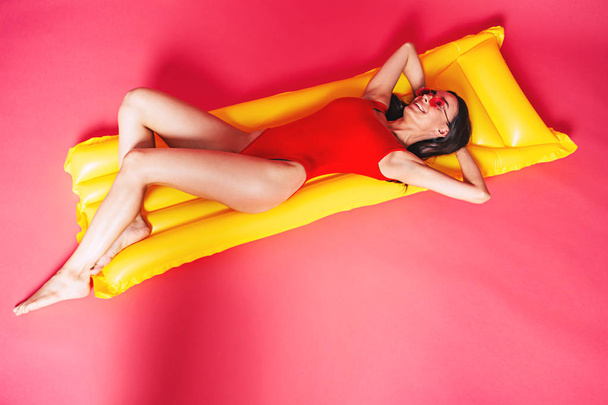 Young woman in red sunglasses posing with air mattress on red background - Фото, зображення